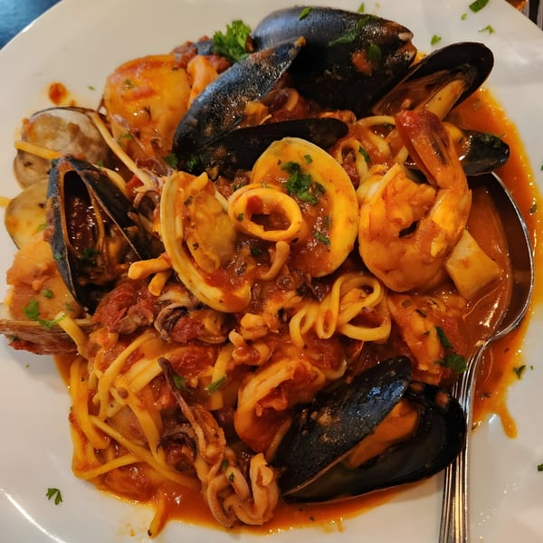 Seafood pasta with mussels, clams, shrimp, and calamari in red sauce on a white plate.