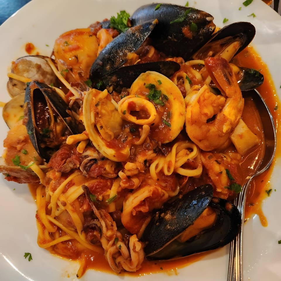 Seafood pasta with mussels, clams, shrimp, and calamari in red sauce on a white plate.