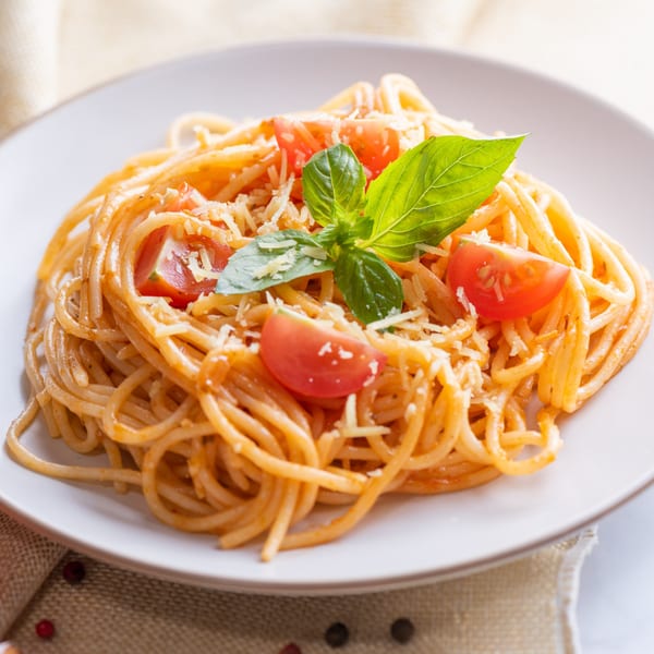 Spaghetti with red sauce, cherry tomatoes, grated cheese, and fresh basil on a white plate.