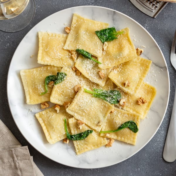 Sarah's on Park's Italian ravioli, topped with parmesan, walnuts, and spinach, on a white marble plate.